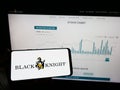 Person holding mobile phone with logo of US financial services company Black Knight Inc. on screen in front of web page.