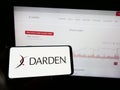 Person holding mobile phone with logo of US gastronomy company Darden Restaurants Inc. on screen in front of web page.