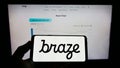 Person holding mobile phone with logo of US marketing software company Braze Inc. on screen in front of business web page.