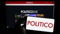 Person holding mobile phone with logo of US political newspaper company Politico LLC on screen in front of web page.