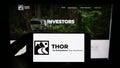 Person holding mobile phone with logo of US RV manufacturing company Thor Industries Inc. on screen in front of web page.