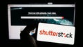 Person holding mobile phone with logo of US stock photography company Shutterstock Inc. on screen in front of web page.