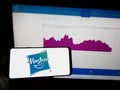 Person holding mobile phone with logo of US toys and entertainment company Hasbro Inc. on screen in front of web page.