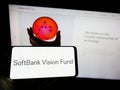 Person holding mobile phone with logo of venture capital fund SoftBank Vision Fund on screen in front of web page.