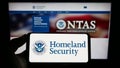 Person holding mobile phone with seal of American Department of Homeland Security (DHS) on screen in front of web page.