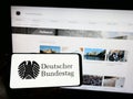 Person holding mobile phone with seal of German federal parliament Bundestag on screen in front of web page.