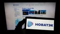 Person holding monbile phone with logo of Russian natural gas company Novatek on screen in front of business web page.