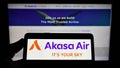 Person holding smartphone with logo of airline SNV Aviation Private Limited (Akasa Air) on screen in front of website.