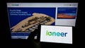 Person holding smartphone with logo of Australian mining company company ioneer Ltd. on screen in front of website.