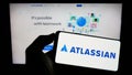 Person holding smartphone with logo of Australian software company Atlassian Corporation on screen in front of website.