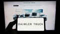 Person holding smartphone with logo of automotive company Daimler Truck Holding AG on screen in front of website.