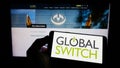 Person holding smartphone with logo of British data center company Global Switch Limited on screen in front of web page.