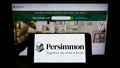 Person holding smartphone with logo of British housebuilding company Persimmon plc on screen in front of website.