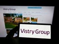 Person holding smartphone with logo of British housebuilding company Vistry Group plc on screen in front of website.