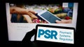 Person holding smartphone with logo of British Payment Systems Regulator (PSR) on screen in front of website. Royalty Free Stock Photo