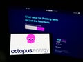 Person holding smartphone with logo of British renewables company Octopus Energy Group on screen in front of website.