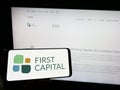 Person holding smartphone with logo of Canadian real estate company First Capital REIT on screen in front of website.