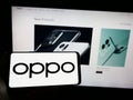 Person holding smartphone with logo of Chinese consumer electronics company OPPO on screen in front of website.