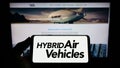 Person holding smartphone with logo of company Hybrid Air Vehicles Limited (HAV) on screen in front of website.