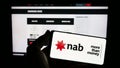 Person holding smartphone with logo of company National Australia Bank Limited (NAB) on screen in front of website.