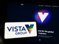 Person holding smartphone with logo of company Vista Group International Limited on screen in front of website.