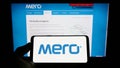 Person holding smartphone with logo of Czech oil pipeline company MERO CR a.s. on screen in front of website.