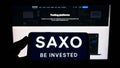 Person holding smartphone with logo of Danish investment banking company Saxo Bank AS on screen in front of website. Royalty Free Stock Photo