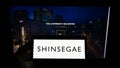 Person holding smartphone with logo of department store company Shinsegae Group on screen in front of website.