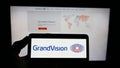 Person holding smartphone with logo of Dutch optical retailing company GrandVision N.V. on screen in front of website.