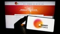 Person holding smartphone with logo of Dutch semiconductor company SMART Photonics B.V. on screen in front of website.