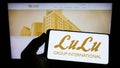 Person holding smartphone with logo of Emirati retail company LuLu Group International on screen in front of website.