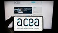 Person holding smartphone with logo of European Automobile Manufacturers Association (ACEA) on screen with website.