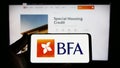 Person holding smartphone with logo of financial company Banco de Fomento Angola (BFA) on screen in front of website.