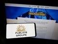 Person holding smartphone with logo of French advertising company Publicis Groupe S.A. on screen in front of website.
