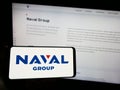 Person holding smartphone with logo of French defense company Naval Group S.A. on screen in front of website.