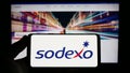 Person holding smartphone with logo of French facility management company Sodexo S.A. on screen in front of website.