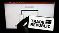 Person holding smartphone with logo of German company Trade Republic Bank GmbH on screen in front of website.