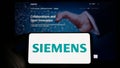 Person holding smartphone with logo of German conglomerate Siemens AG on screen in front of website.