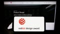 Person holding smartphone with logo of German international prize Red Dot Design Award on screen in front of website.