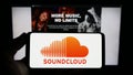 Person holding smartphone with logo of German music sharing company SoundCloud on screen in front of website.