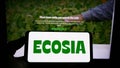 Person holding smartphone with logo of German search engine company Ecosia GmbH on screen in front of website.