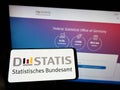 Person holding smartphone with logo of German Statistisches Bundesamt (Destatis) on screen in front of website.