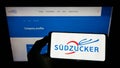 Person holding smartphone with logo of German sugar production company SÃÂ¼dzucker AG on screen in front of website.