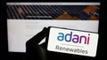 Person holding smartphone with logo of Indian company Adani Green Energy Limited on screen in front of website.