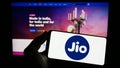 Person holding smartphone with logo of Indian telecommunications company Reliance Jio on screen in front of website.