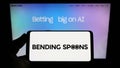 Person holding smartphone with logo of Italian app company Bending Spoons S.p.A. on screen in front of website.