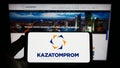 Person holding smartphone with logo of Kazakh uranium mining company Kazatomprom on screen in front of website. Royalty Free Stock Photo