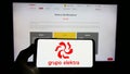 Person holding smartphone with logo of Mexican retail company Grupo Elektra on screen in front of website.