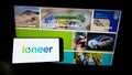 Person holding smartphone with logo of mining company company ioneer Ltd. on screen in front of business webpage.