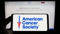 Person holding smartphone with logo of organization American Cancer Society (ACS) on screen in front of website.